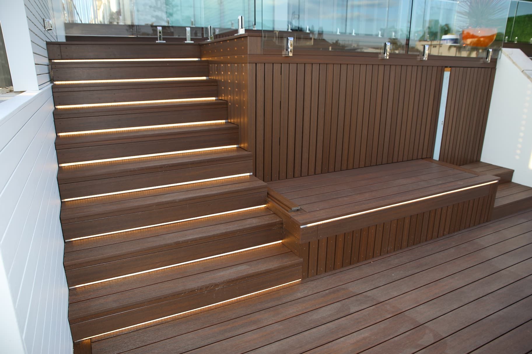 Wooden outdoor stairs and platform with built-in lights and railing. Brown wood with glass.