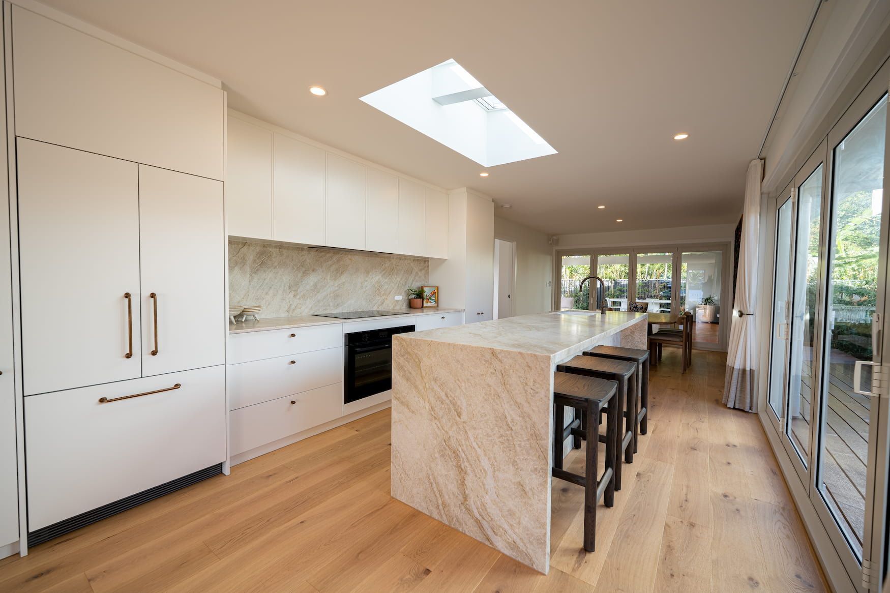 Modern white kitchen with a marble island, wood floors, and large windows.