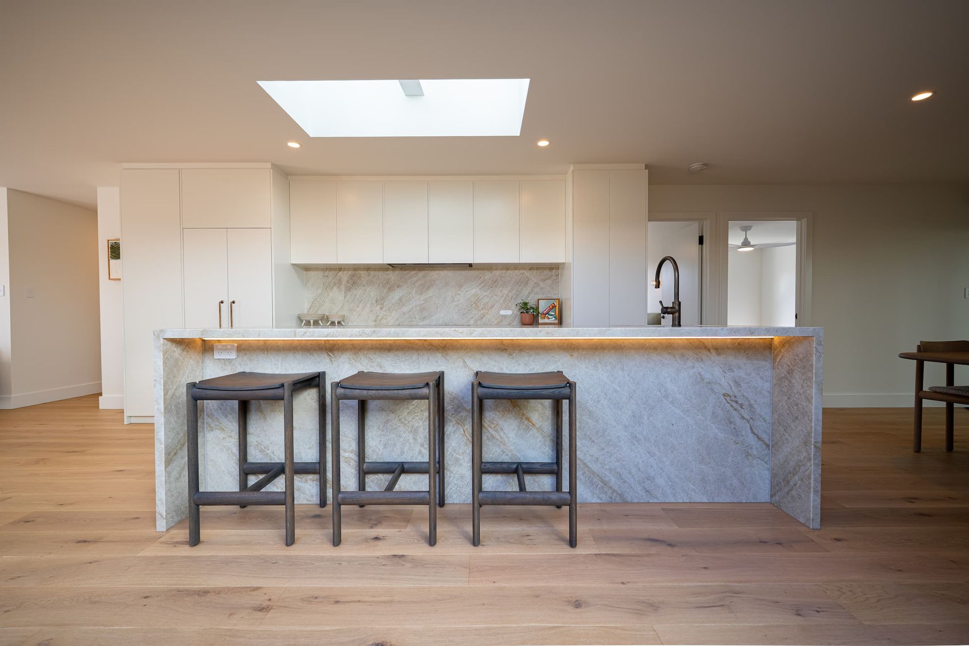 Modern kitchen with marble island, wooden stools, light cabinets, and skylight.