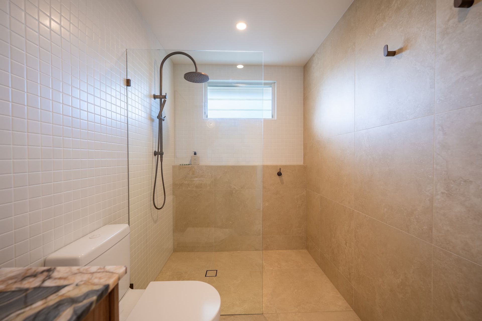 Modern bathroom with white and beige tile, a walk-in shower, and a toilet.