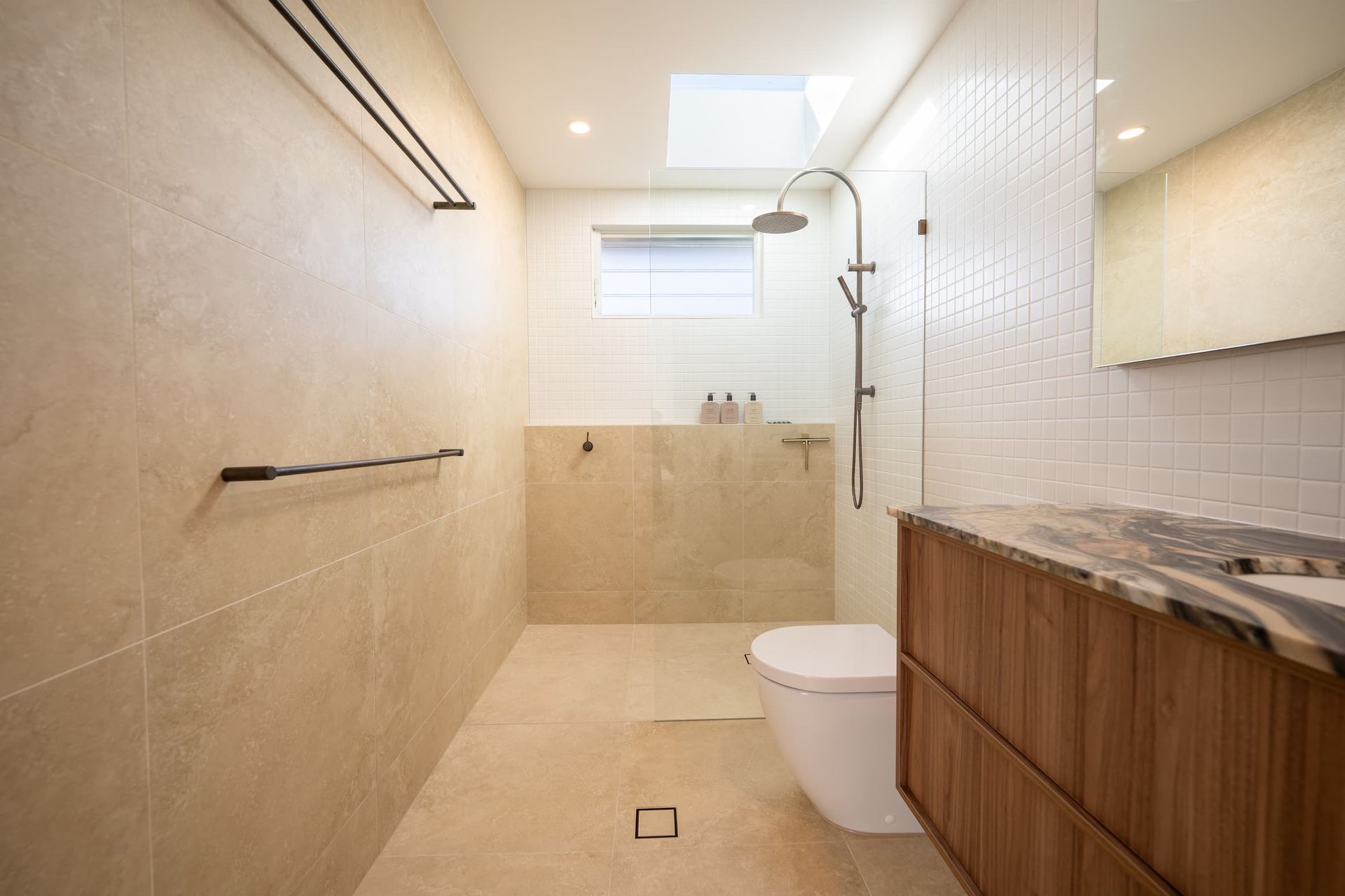 Modern bathroom with beige tile, wood vanity, and white fixtures.