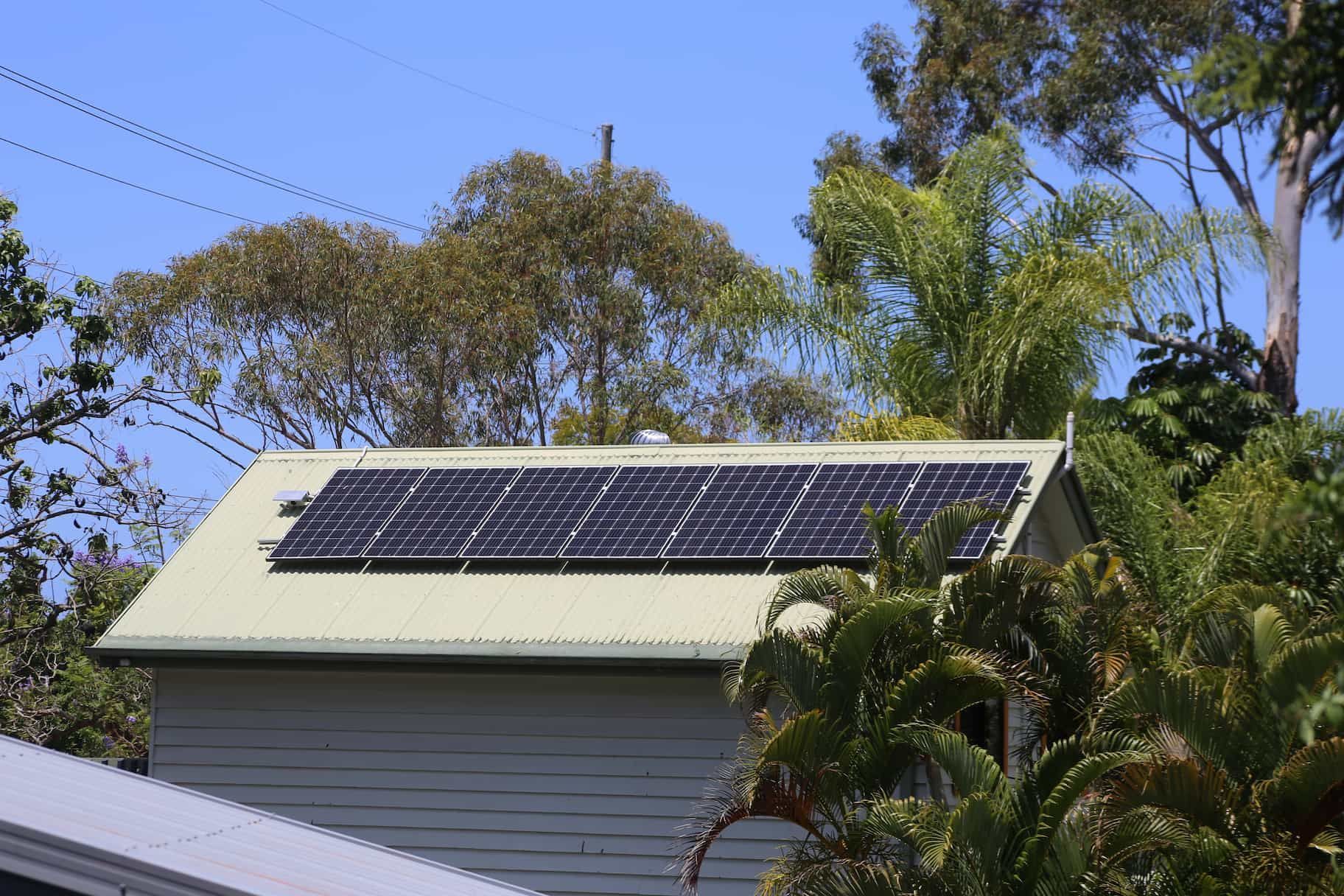 Several solar panels on a green roof with trees in the background 