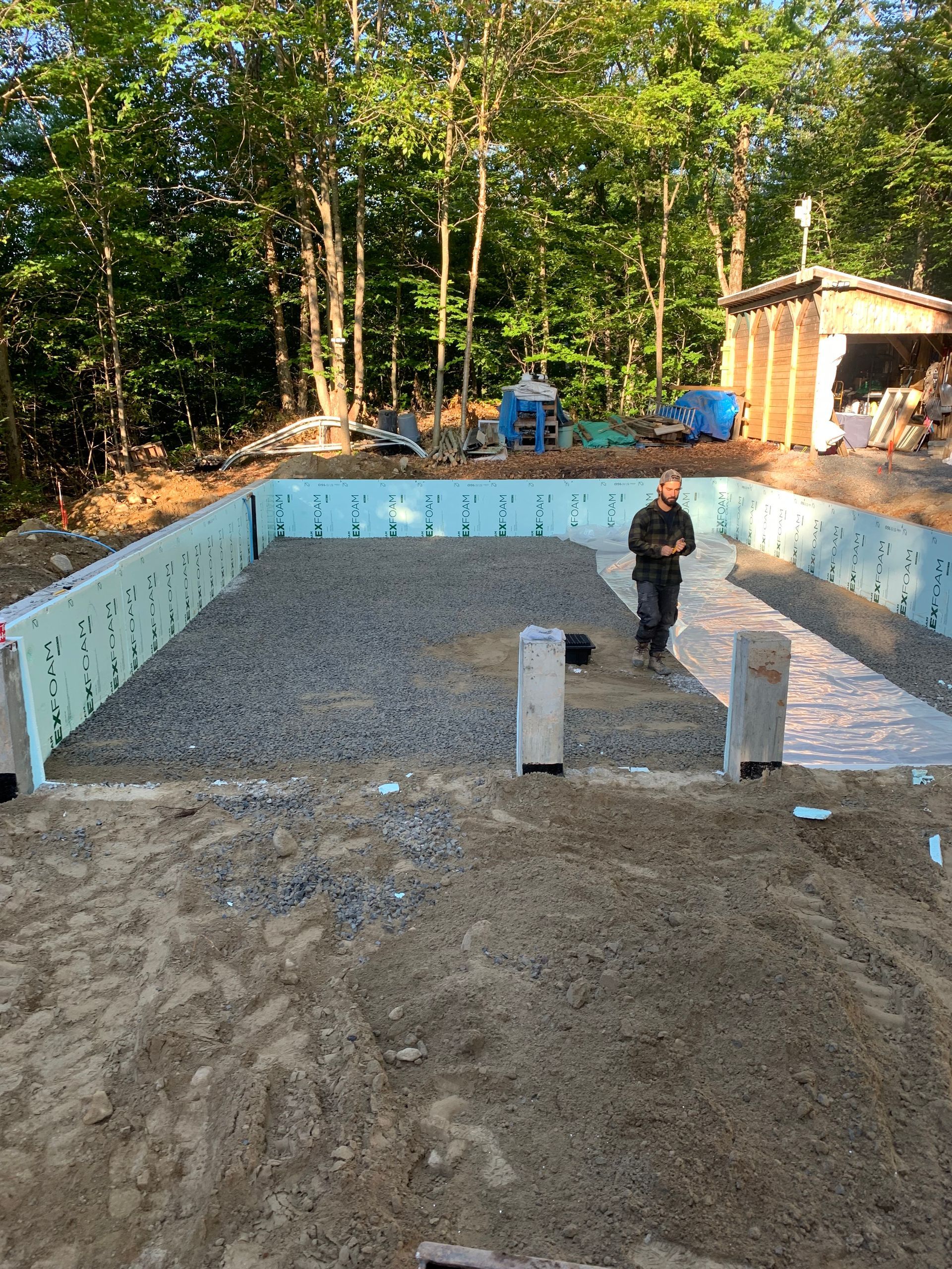 Une personne se tient à l'intérieur d'une fondation rectangulaire aux murs isolés bleu clair, au sol recouvert de gravier et aux piliers en béton.