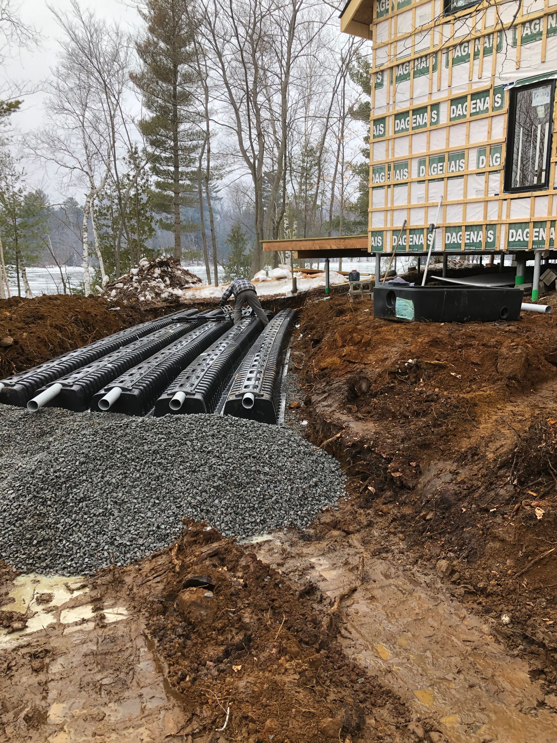 Un champ d'épandage septique en construction, avec des rangées de chambres en plastique installées dans une tranchée remplie de gravier près d'une maison.