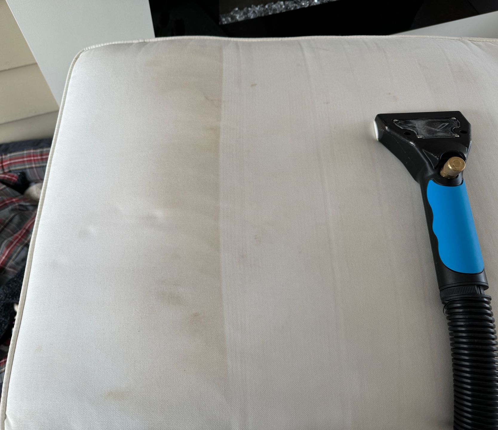 A person is cleaning a couch with a vacuum cleaner.