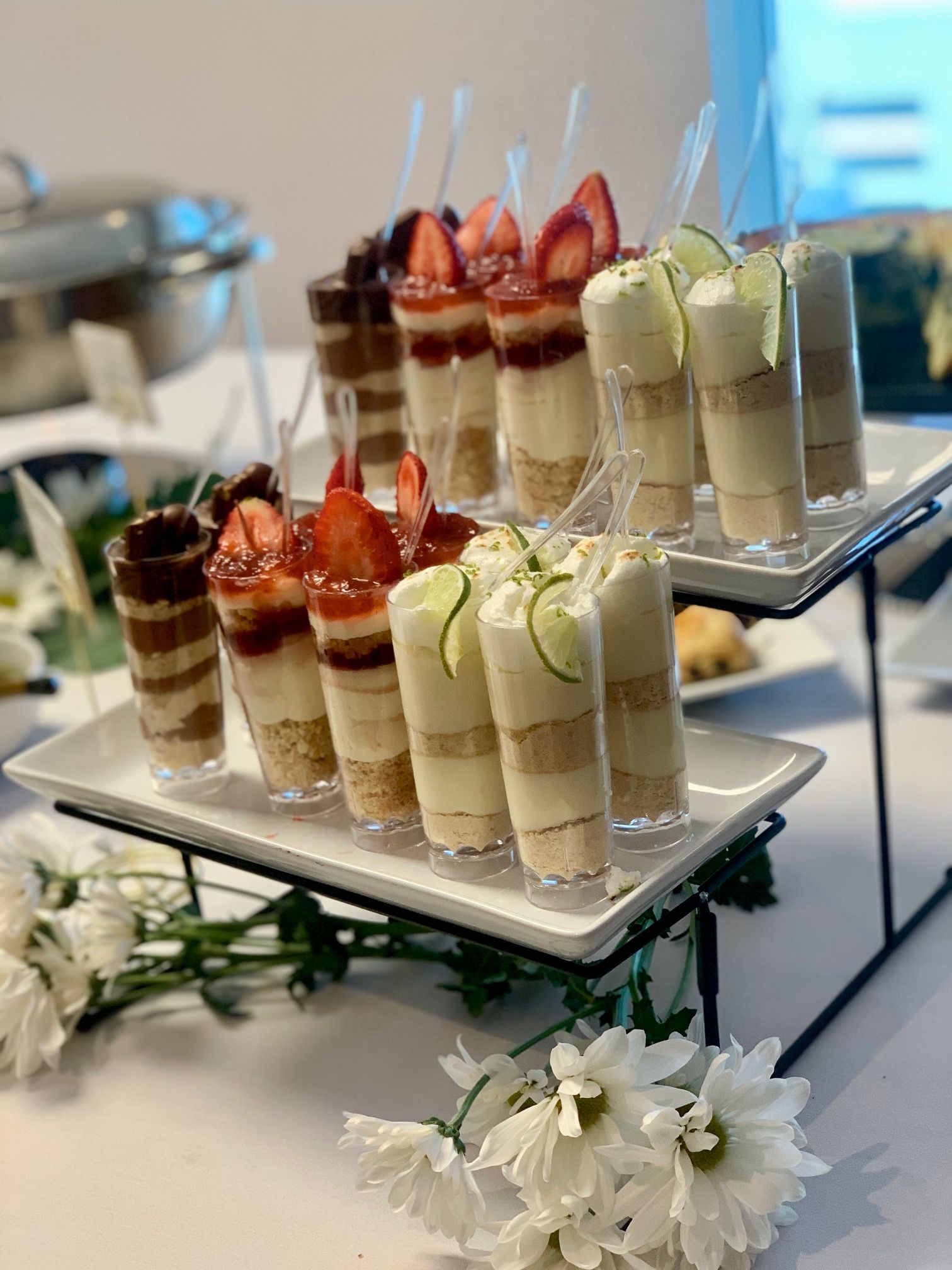Tiered plates of mini dessert parfaits topped with strawberries and cream, arranged with white flowers