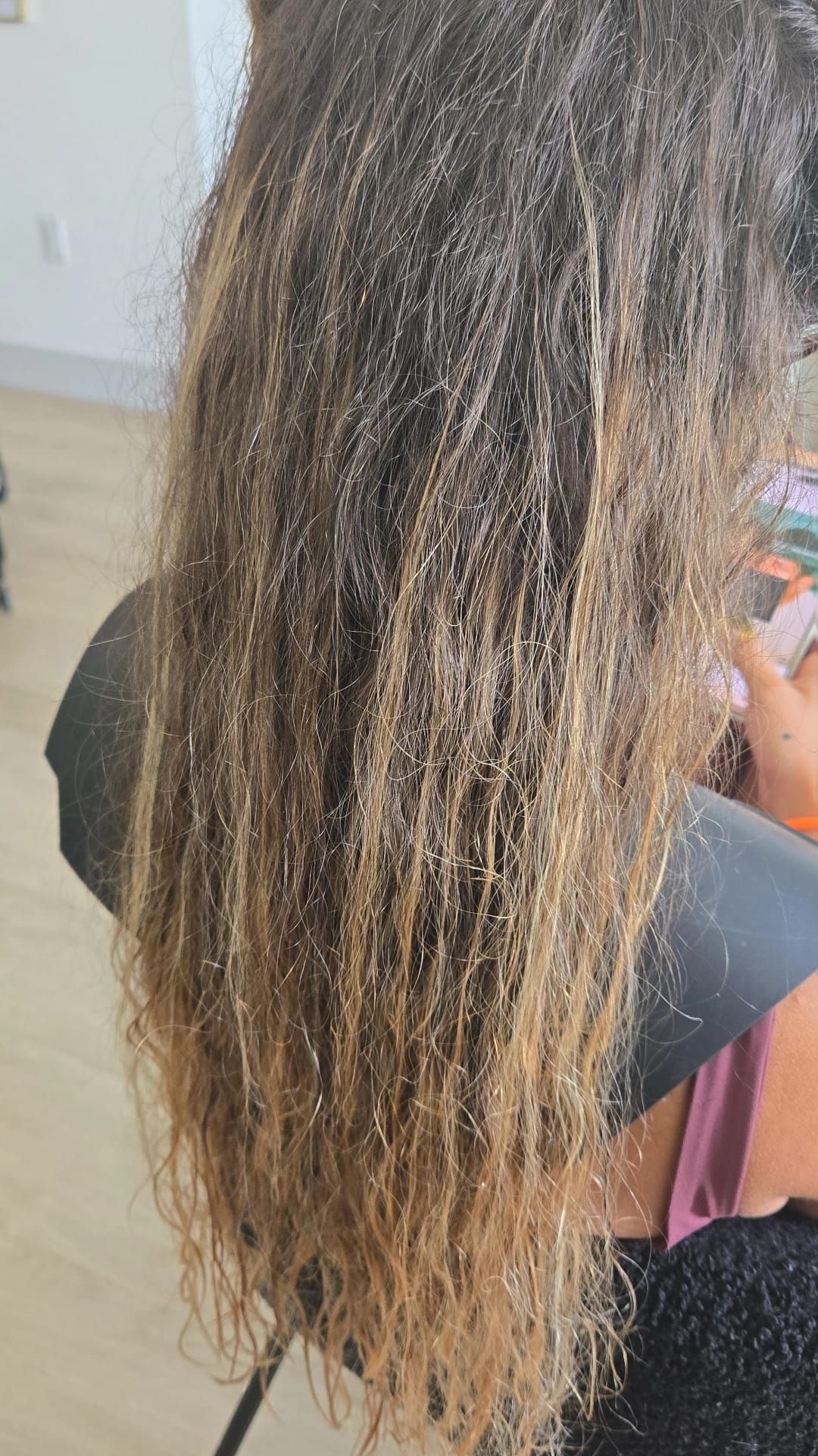 Back view of long, wavy brown hair with blonde ends, resting over a black shirt.