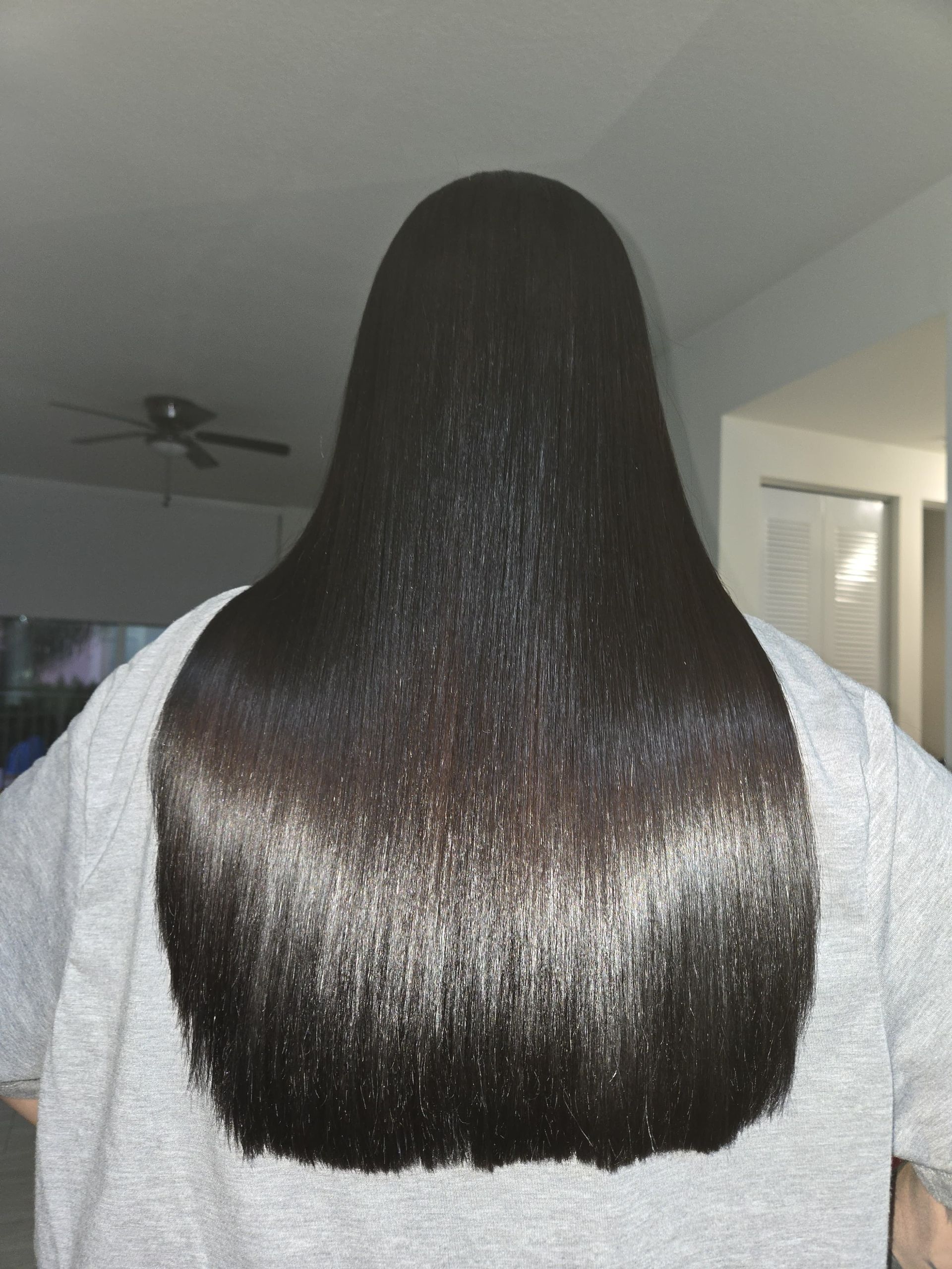 Person with long, straight black hair standing indoors, back facing camera.