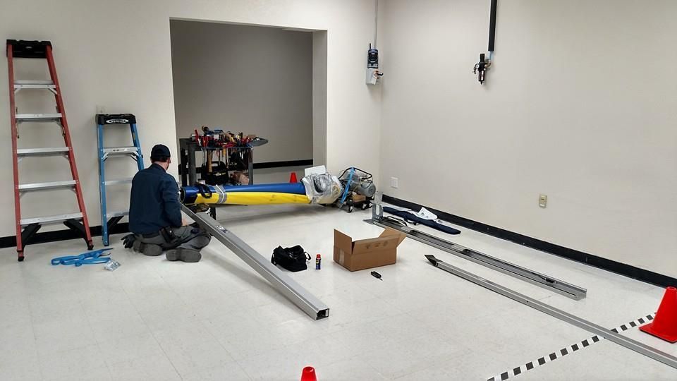 A person assembling equipment in a room with tools, a ladder, and a partially constructed machine.