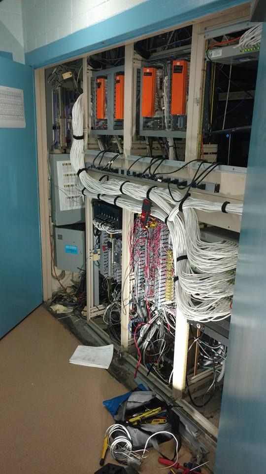 Open cabinet with orange-boxed electronics and tangled wires; a construction or service setting.