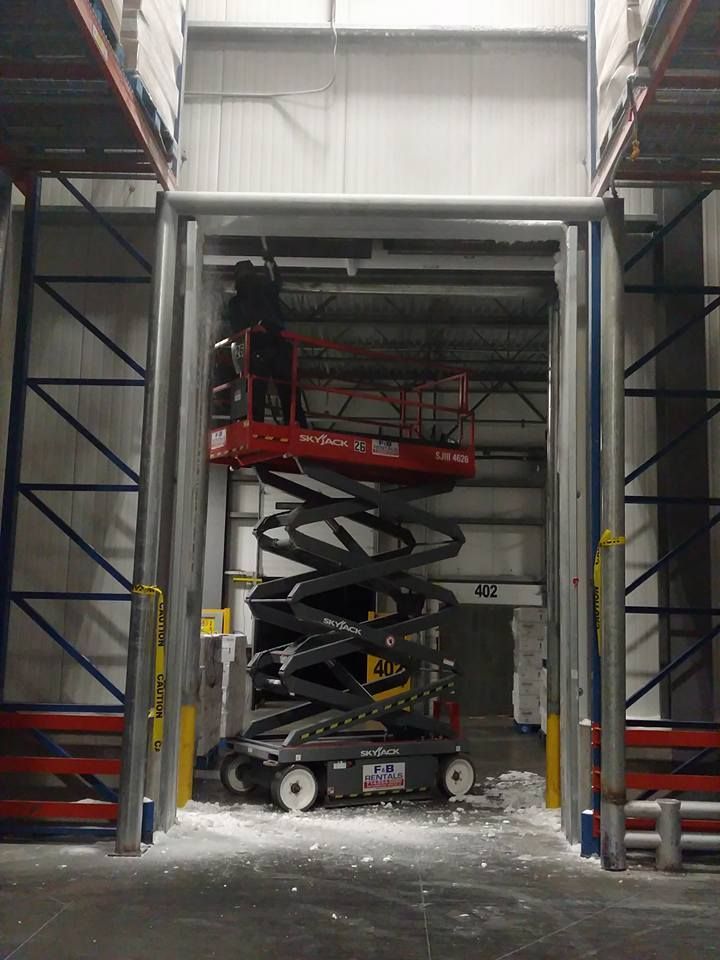 A scissor lift inside a warehouse doorway; a person is in the lift's basket.