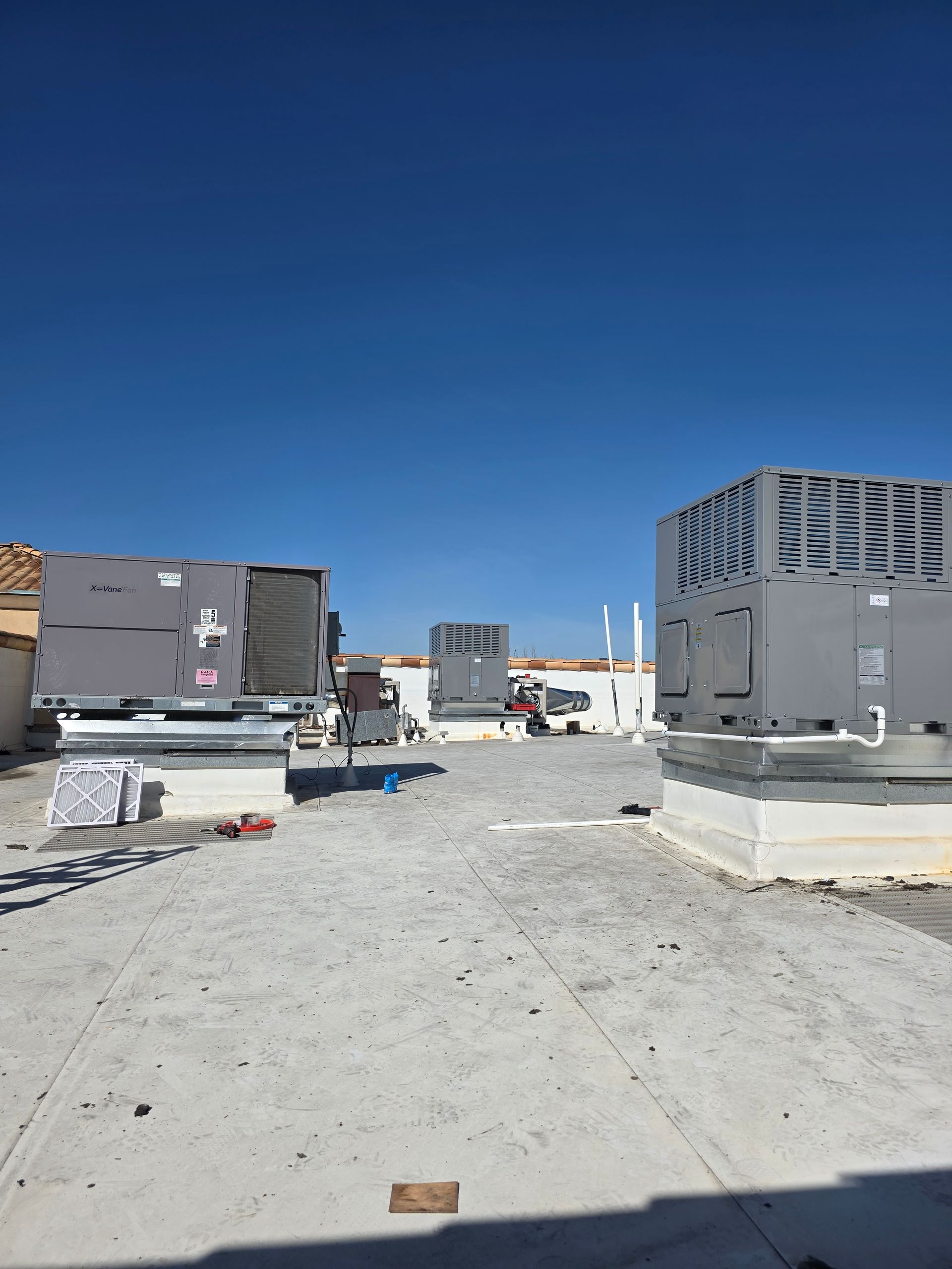 Rooftop with HVAC units, construction materials, and a clear blue sky.