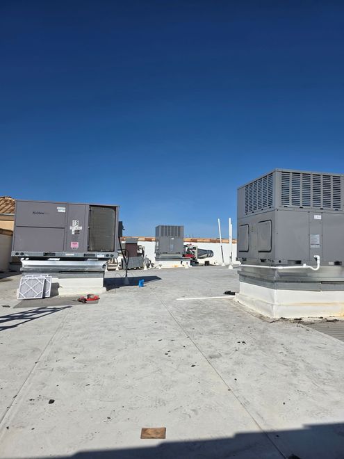 Rooftop with HVAC units, construction materials, and a clear blue sky.