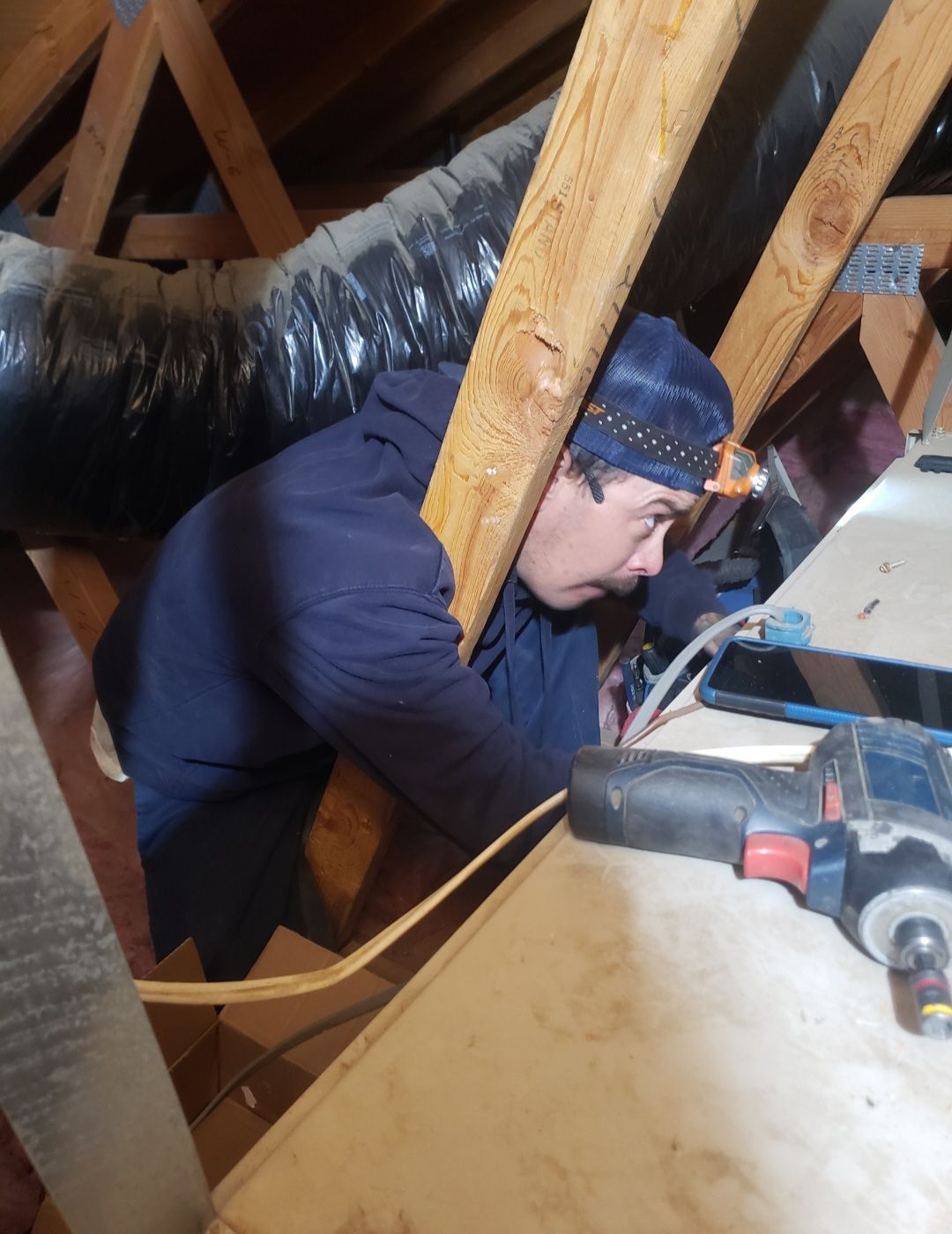 Person in blue jacket and beanie working in an attic with tools and exposed rafters