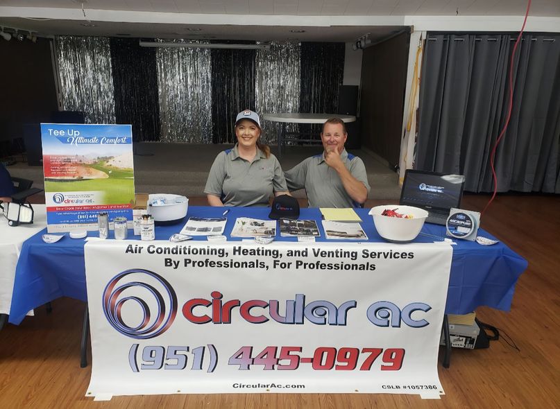 Two people behind a blue Circular AC service booth with laptop and sign in a hall
