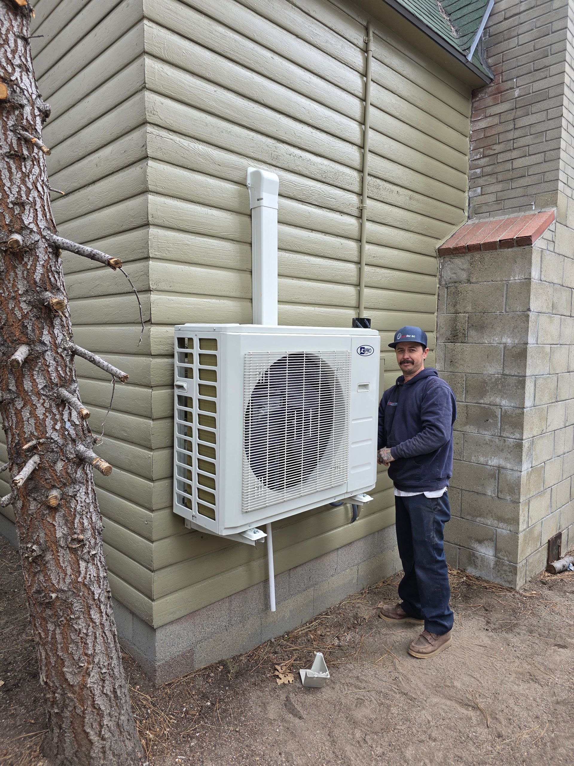 Outdoor HVAC unit mounted on a wall beside a worker in a blue jacket and cap