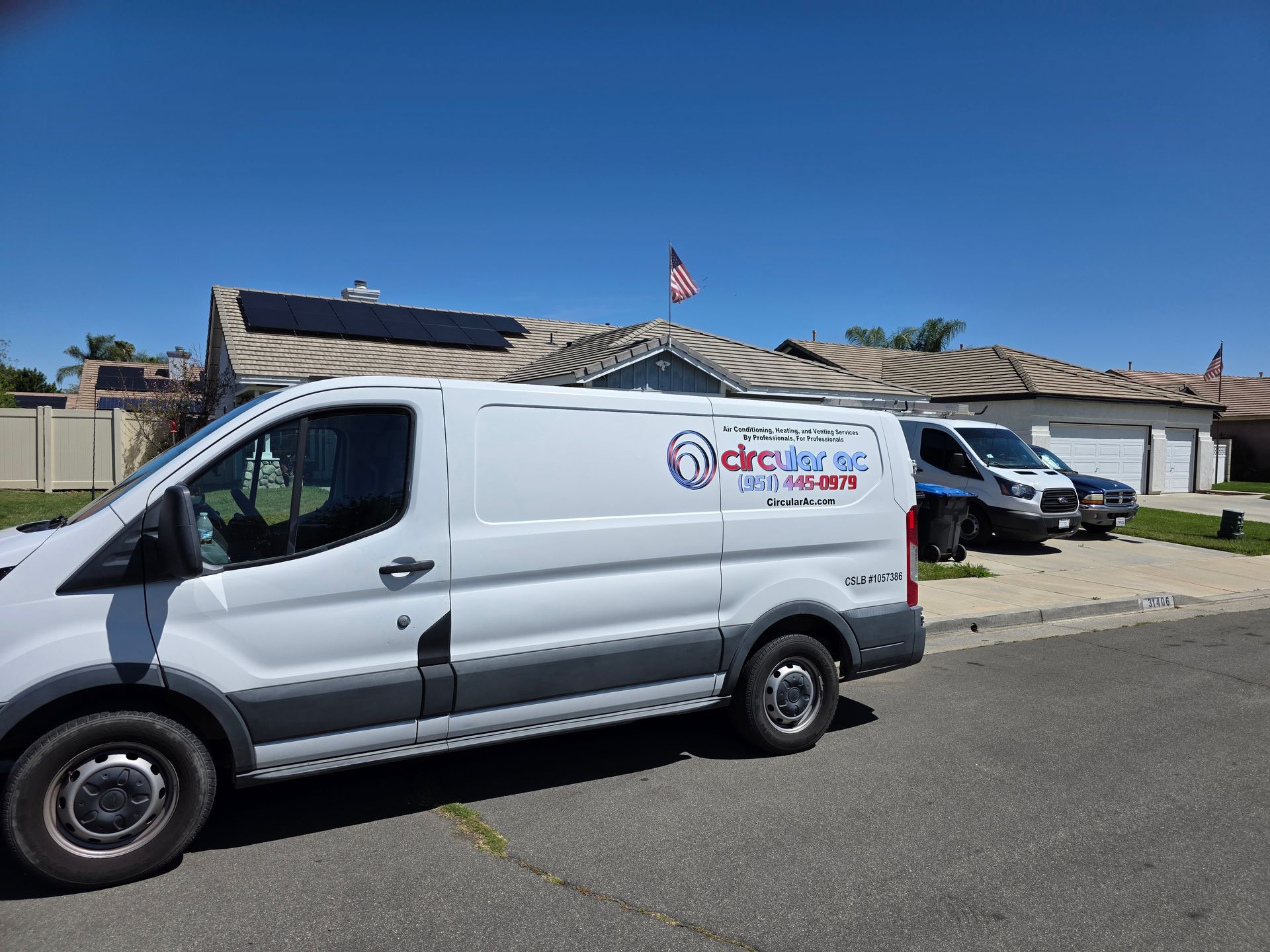 White service van parked outside a low building under a blue sky, with a U.S. flag in the background.