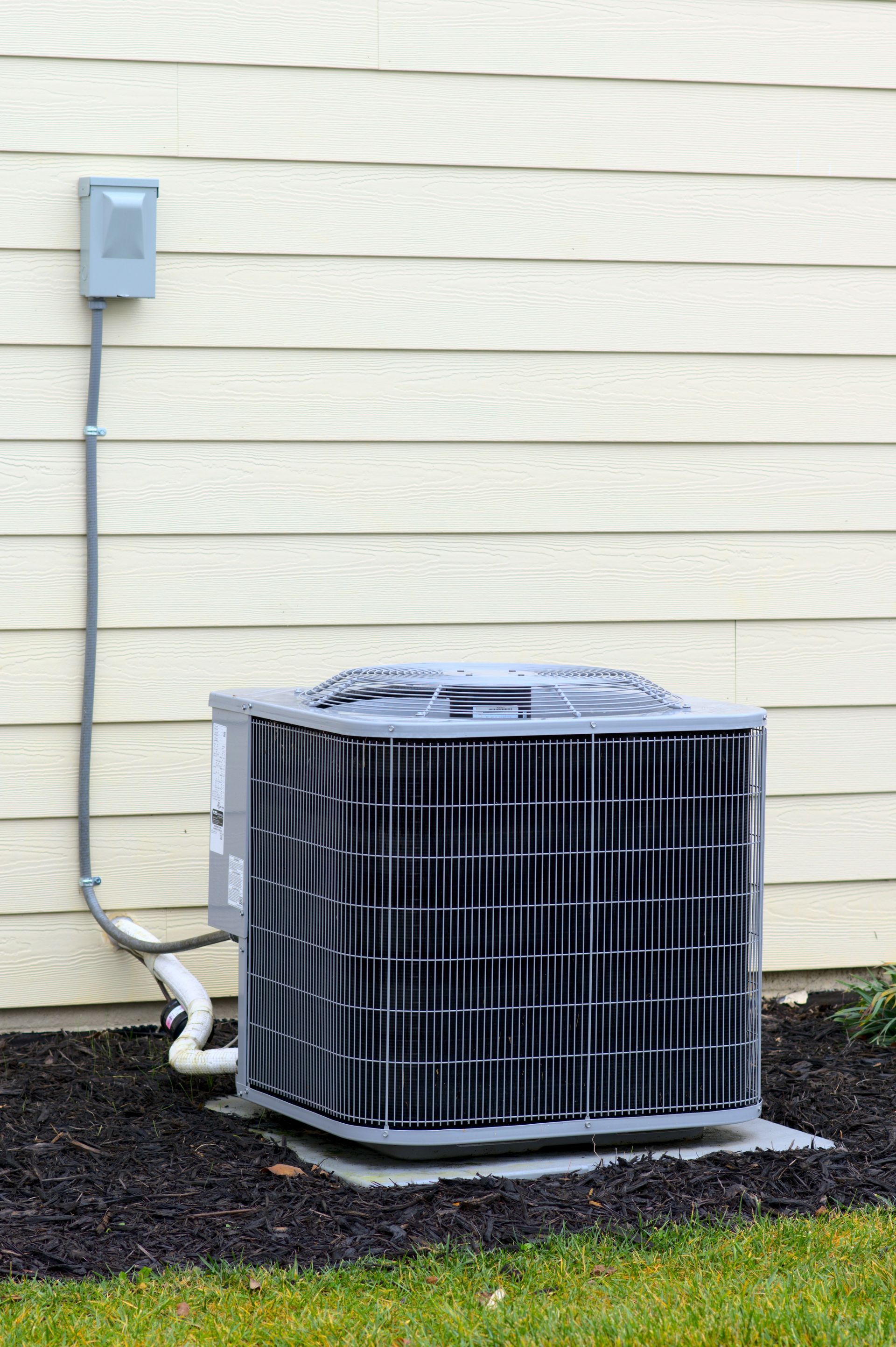 Outdoor air conditioner unit beside beige siding with electrical box and conduit