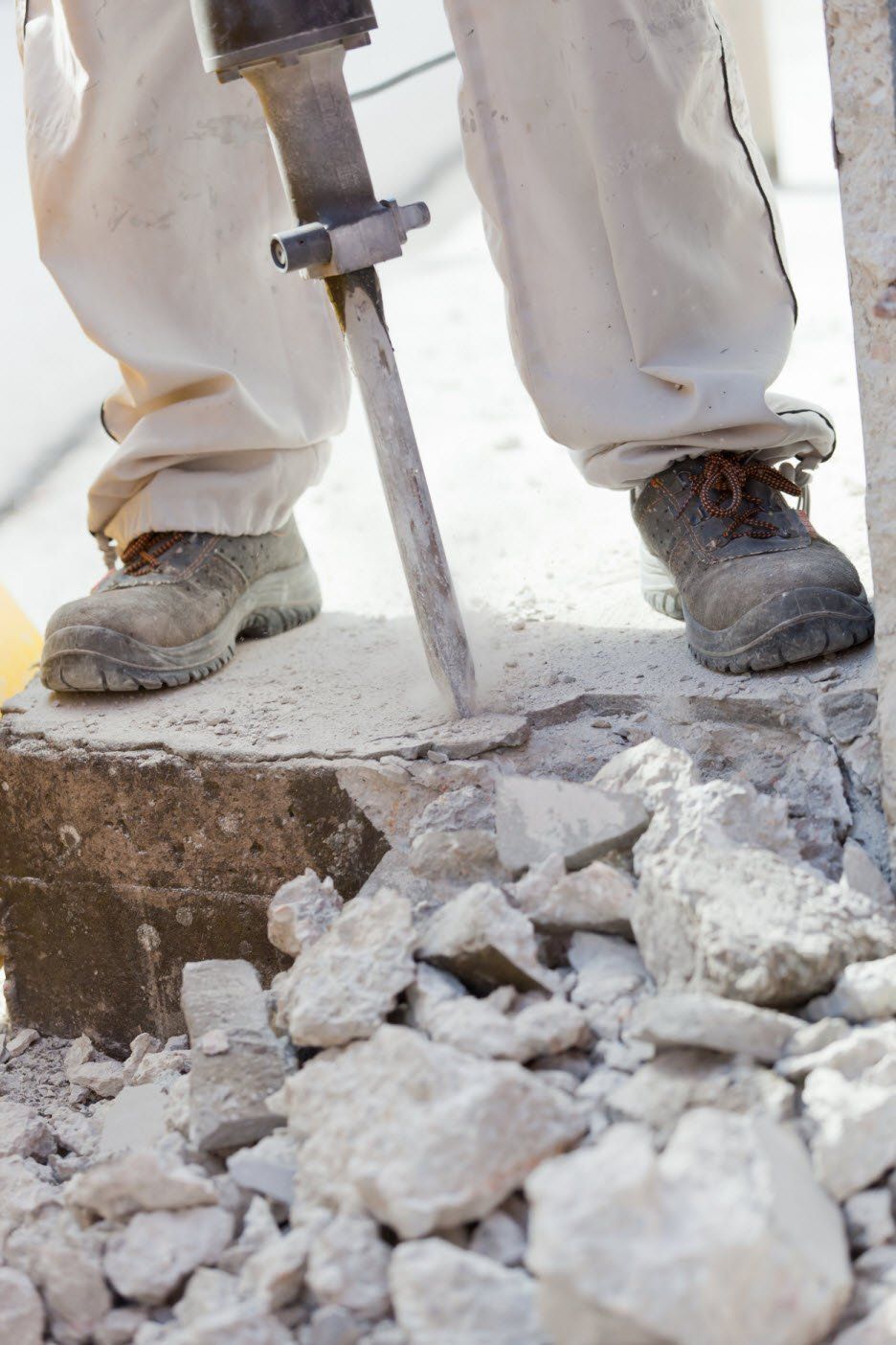 Person in work boots using a jackhammer to break concrete, construction site.
