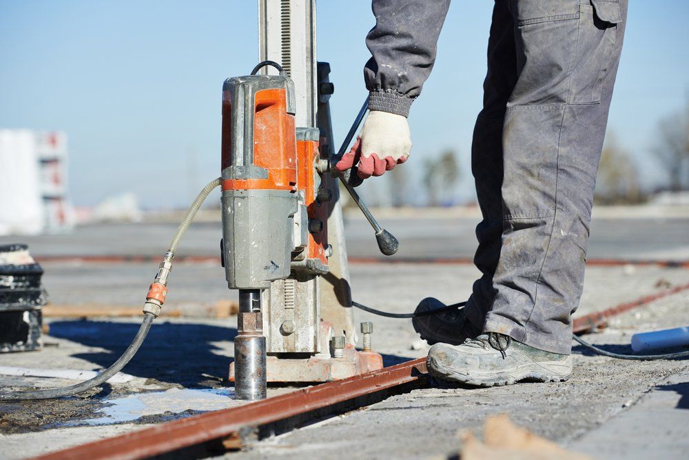 Person using a coring drill on concrete outdoors.