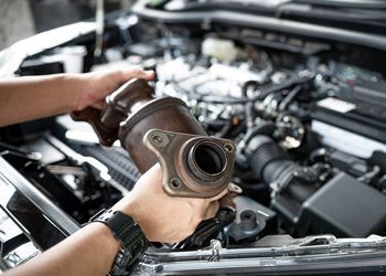 A person is holding a piece of metal in front of a car engine.