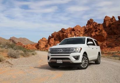 A white suv is parked on a dirt road in the desert.