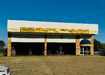 A car is parked in front of a building that says mufflers and brakes.