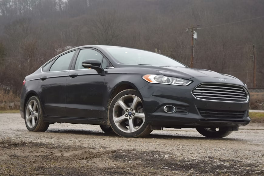 Dark gray Ford Fusion sedan parked on a dirt road against a cloudy sky.