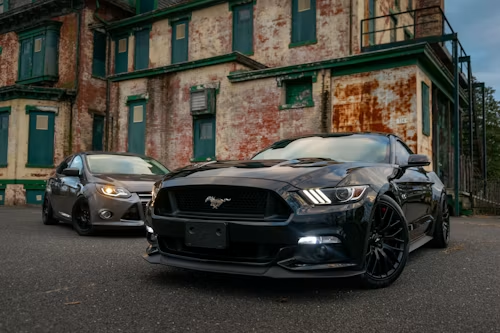 Two black Ford Mustang cars parked in front of an old brick building at dusk