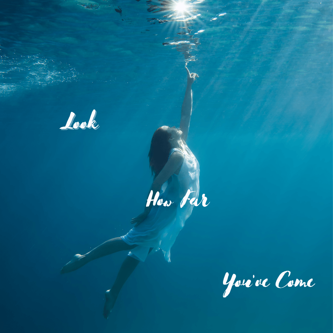 a woman under water readhing up to the light at the surface