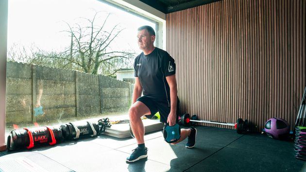 Een man doet lunges met een halter in een sportschool.
