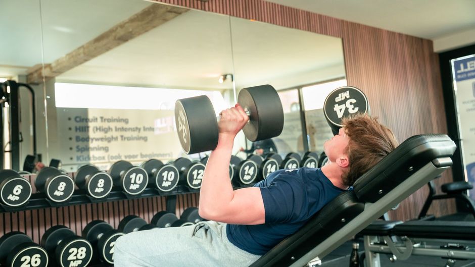 Een man tilt een halter op een bankje in een sportschool.