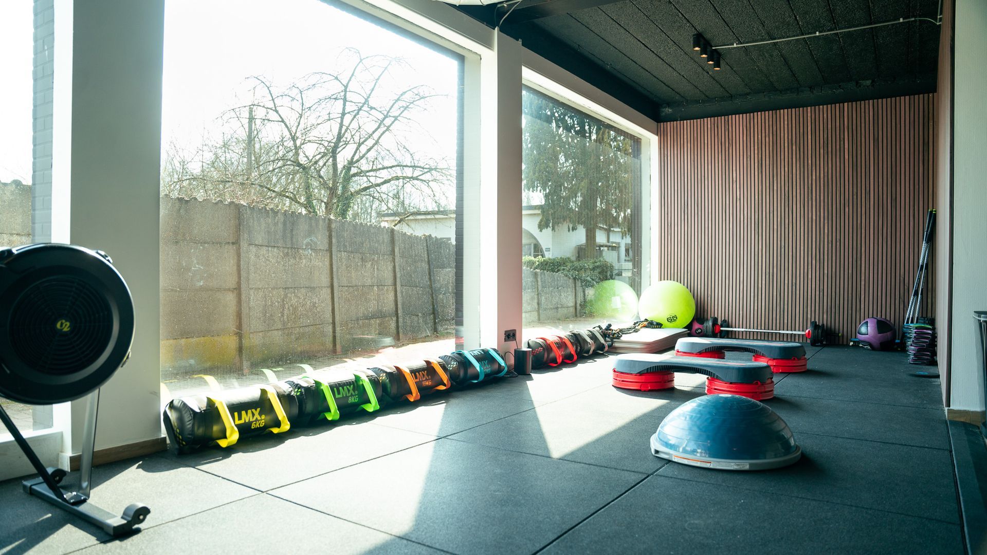Een sportschool met veel fitnessapparatuur en een groot raam.