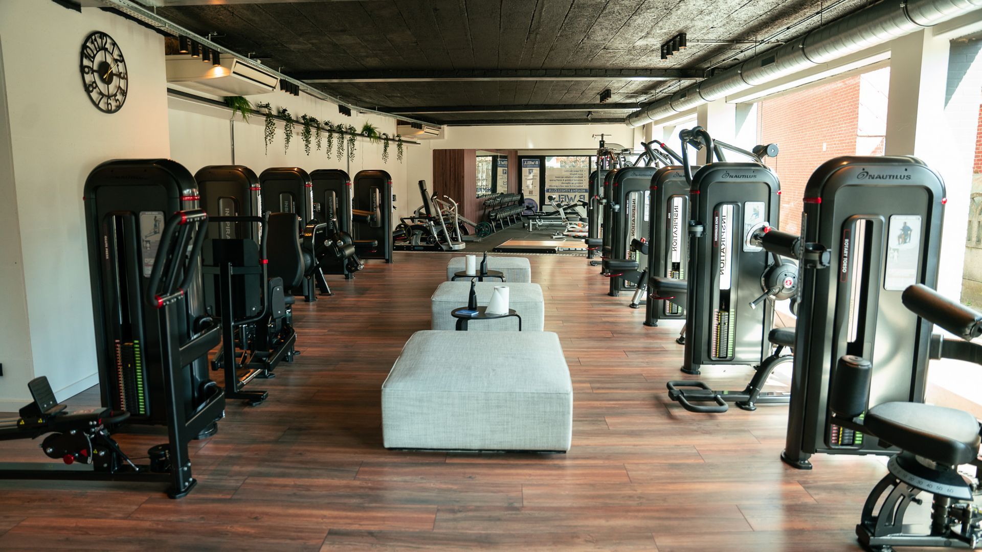 Een sportschool vol met fitnessapparatuur en een klok aan de muur.