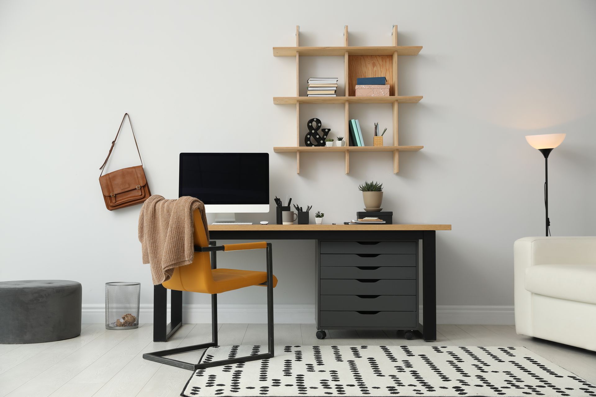Minimal home office with desk, laptop, shelves, floor lamp, chair, rug, and beige sofa