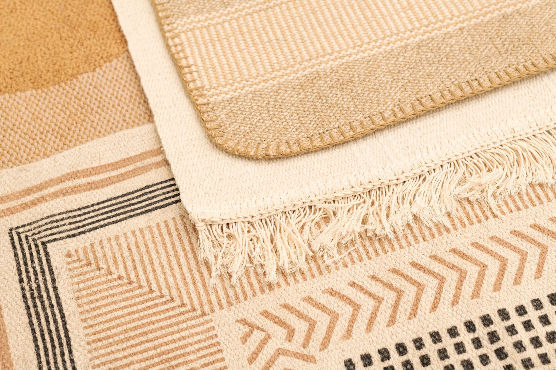 Beige woven rugs and textured fabric mats layered with fringe and geometric patterns
