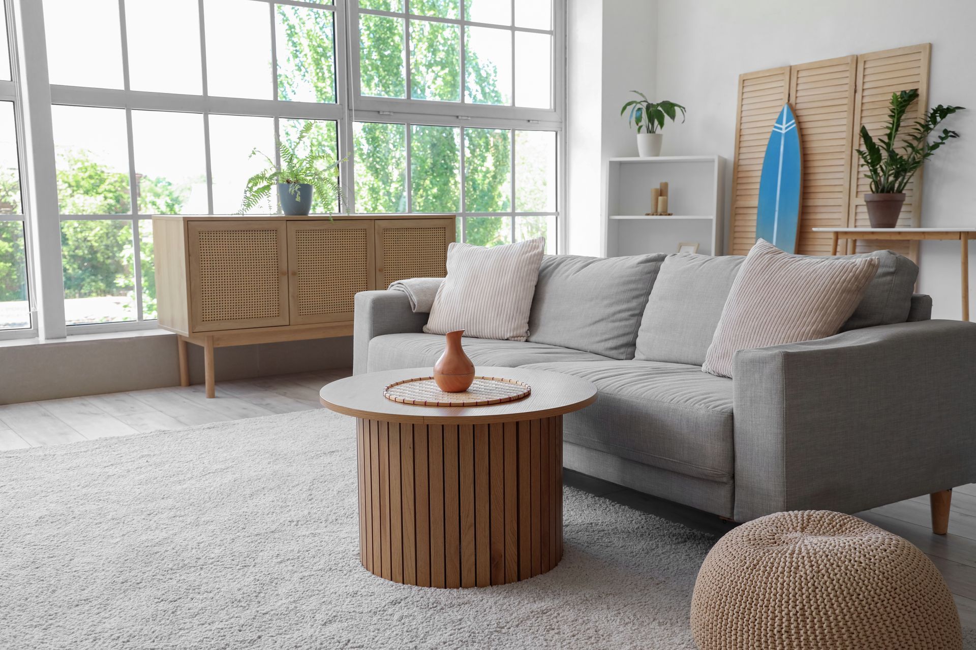 Bright living room with gray sofa, round wood coffee table, and large windows.