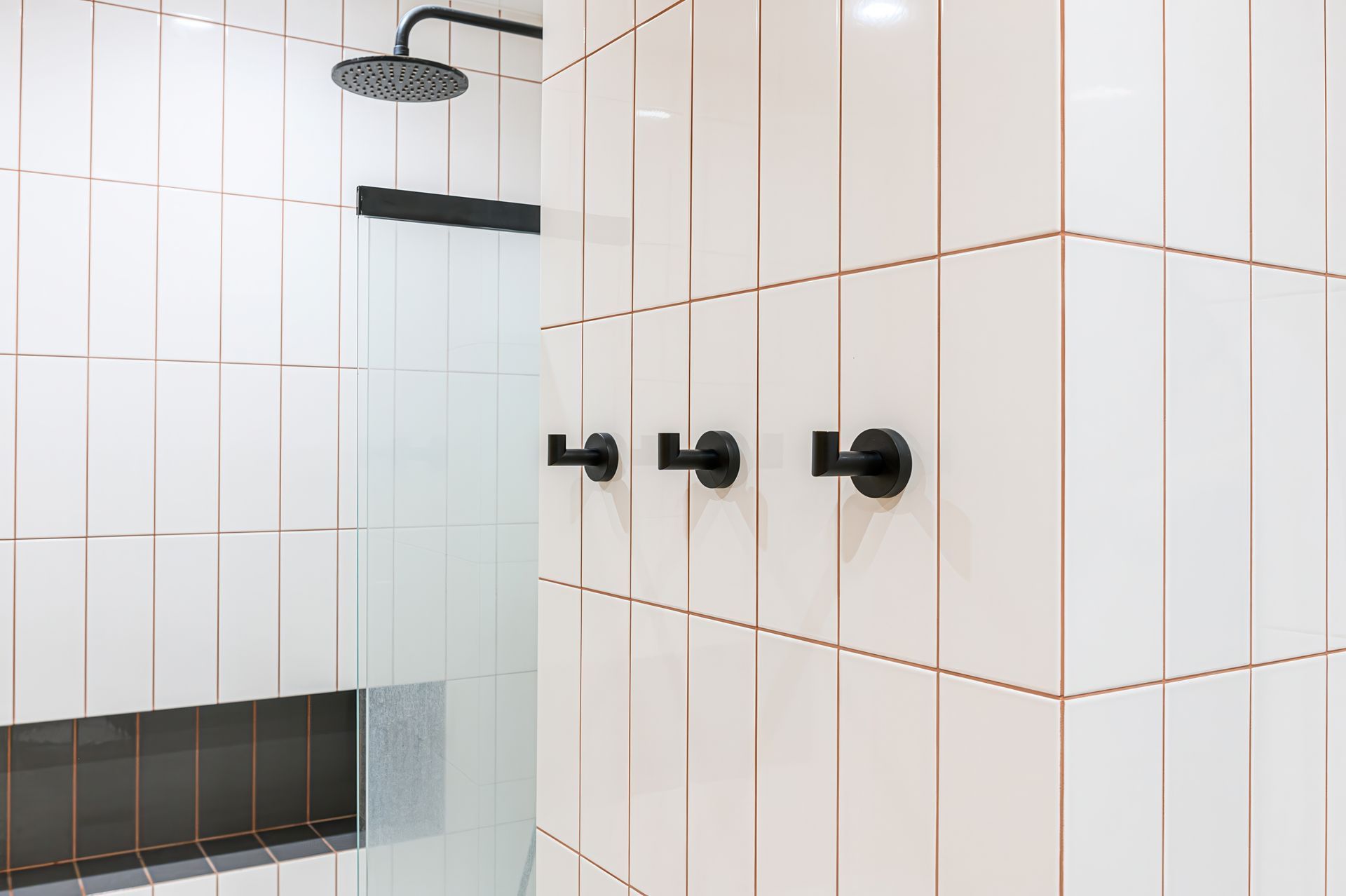 Modern shower with white tile walls, black fixtures, and a glass divider