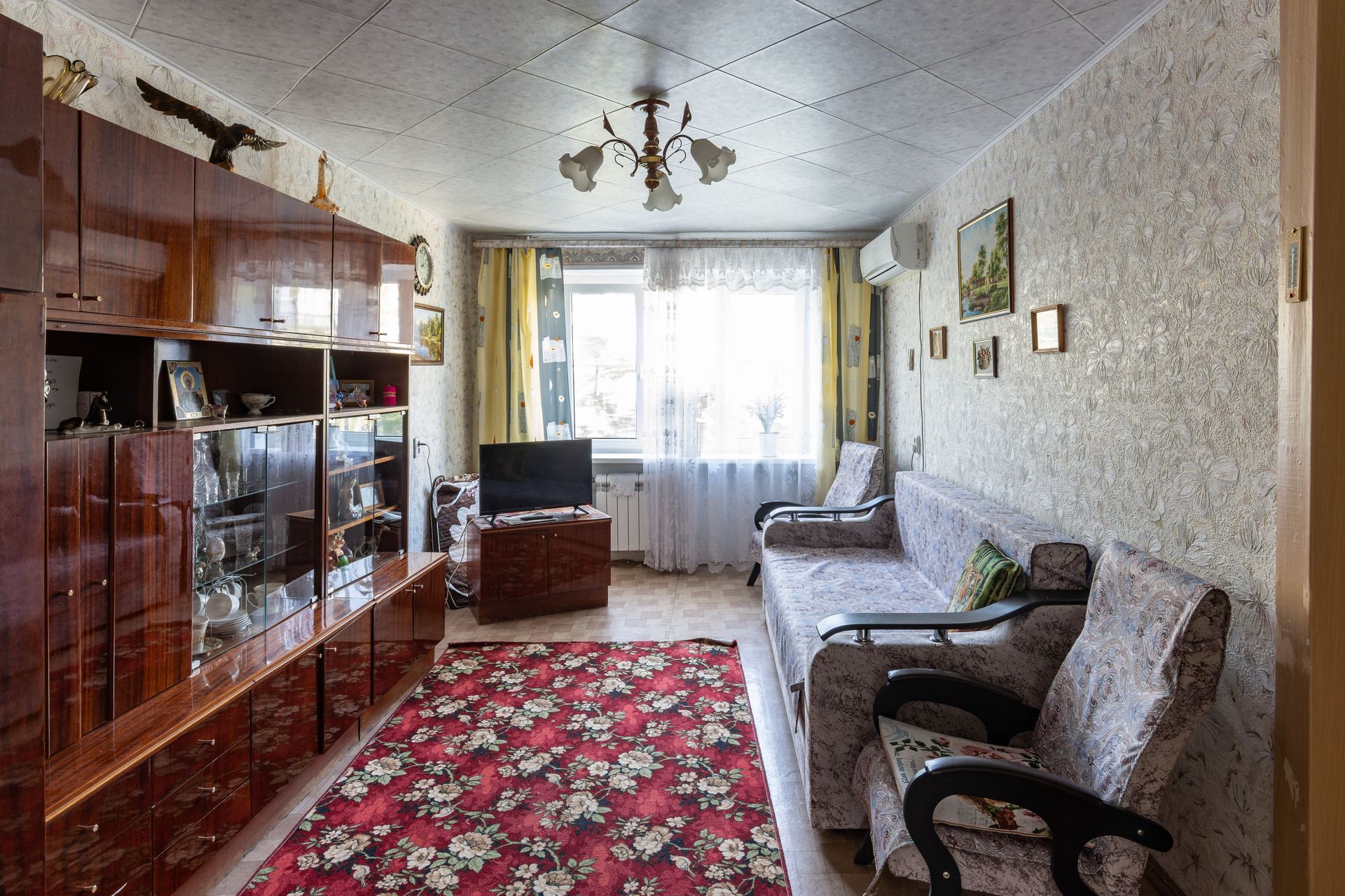 Cozy living room with red patterned rug, sofas, wooden cabinet, and bright window curtains