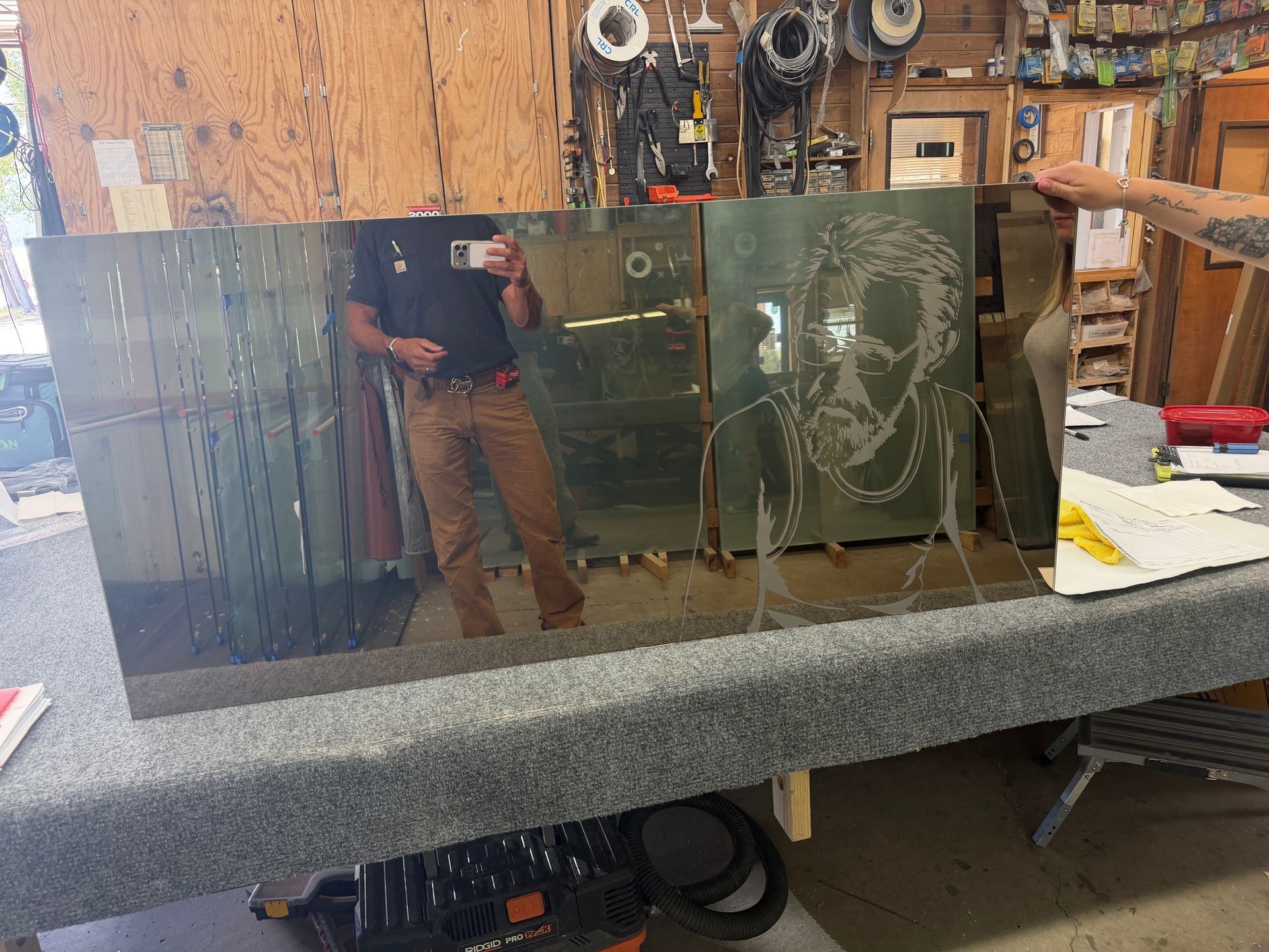 Reflective glass panel with etched swirls on a workbench in a cluttered workshop