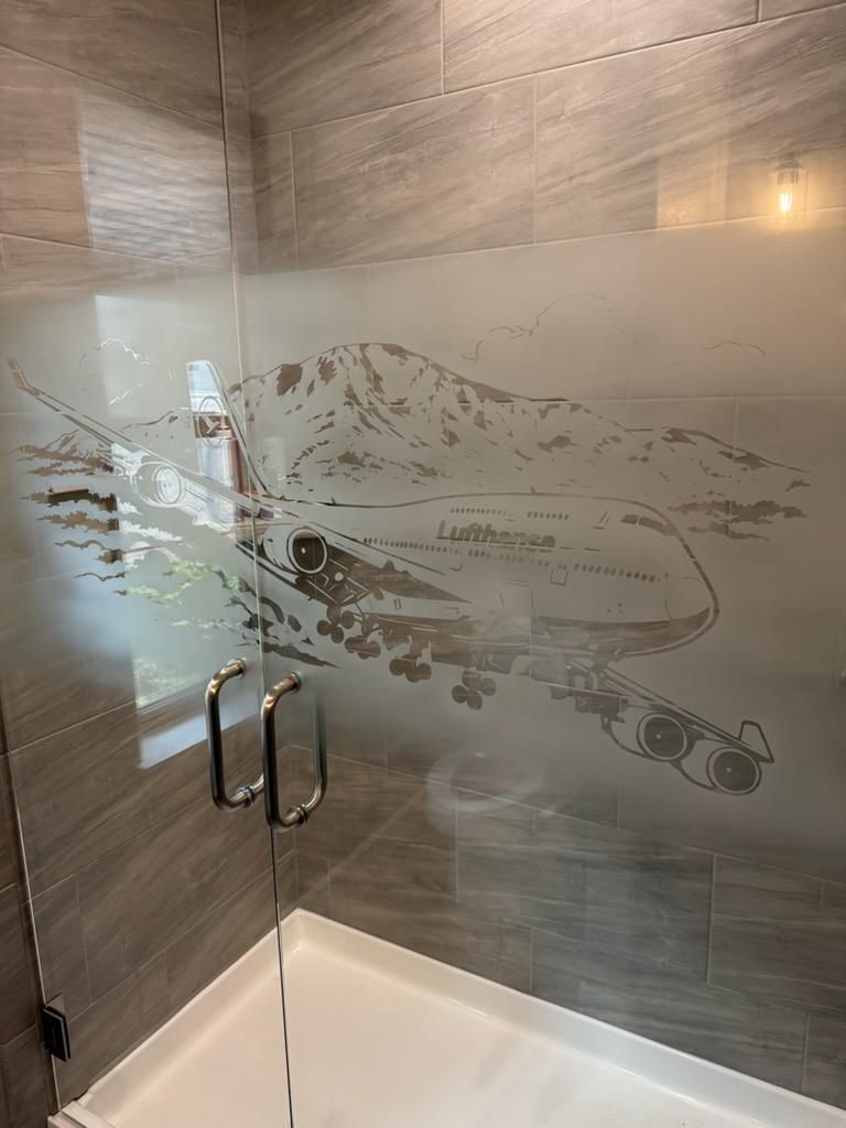 Glass shower enclosure with frosted fish design and chrome handles in a tiled bathroom