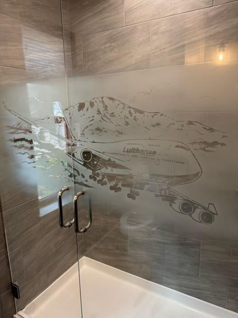 Frosted glass shower enclosure with etched fish design and chrome handles in a tiled bathroom