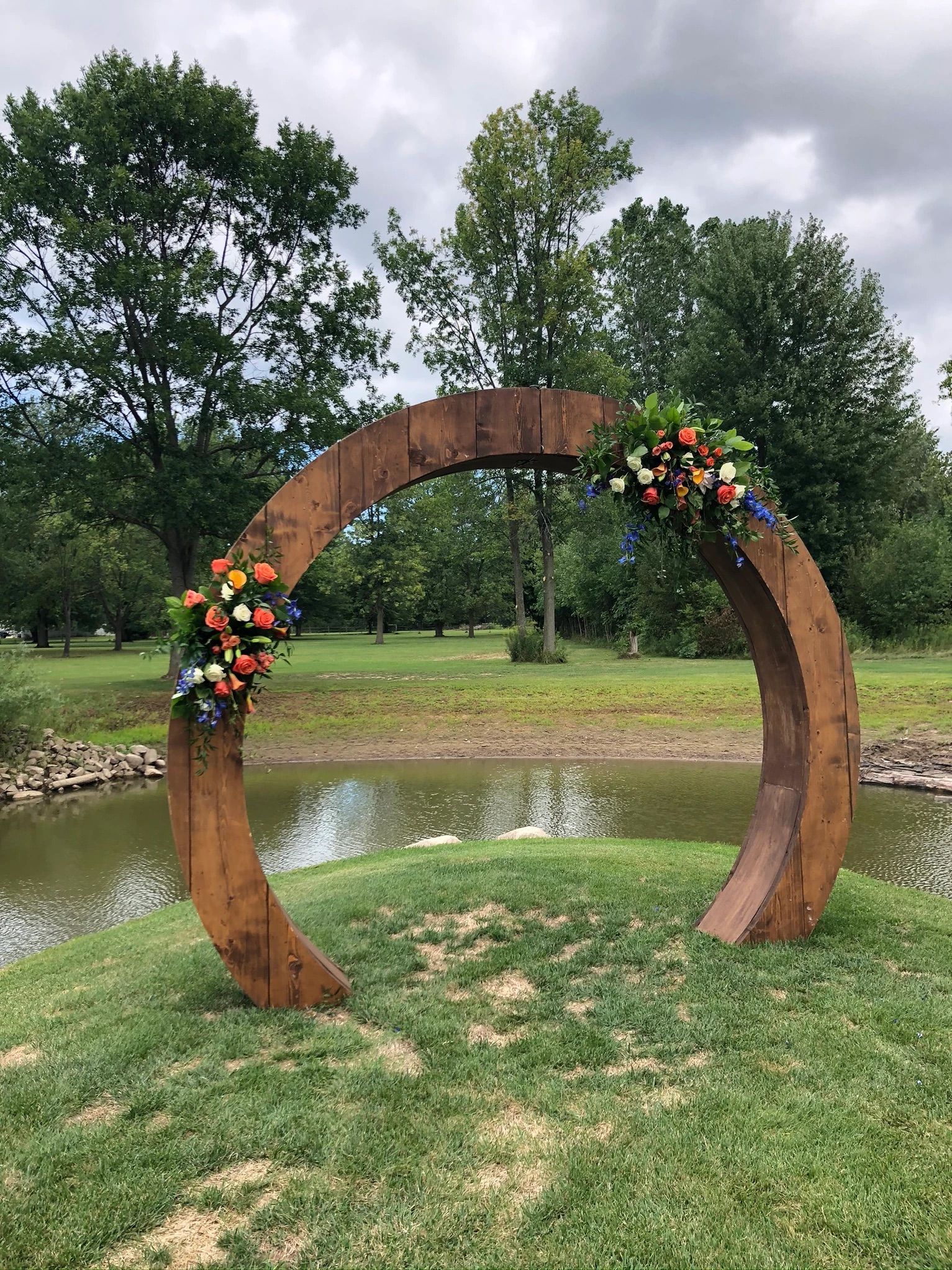 A wooden arch decorated with flowers is sitting in the grass next to a pond.