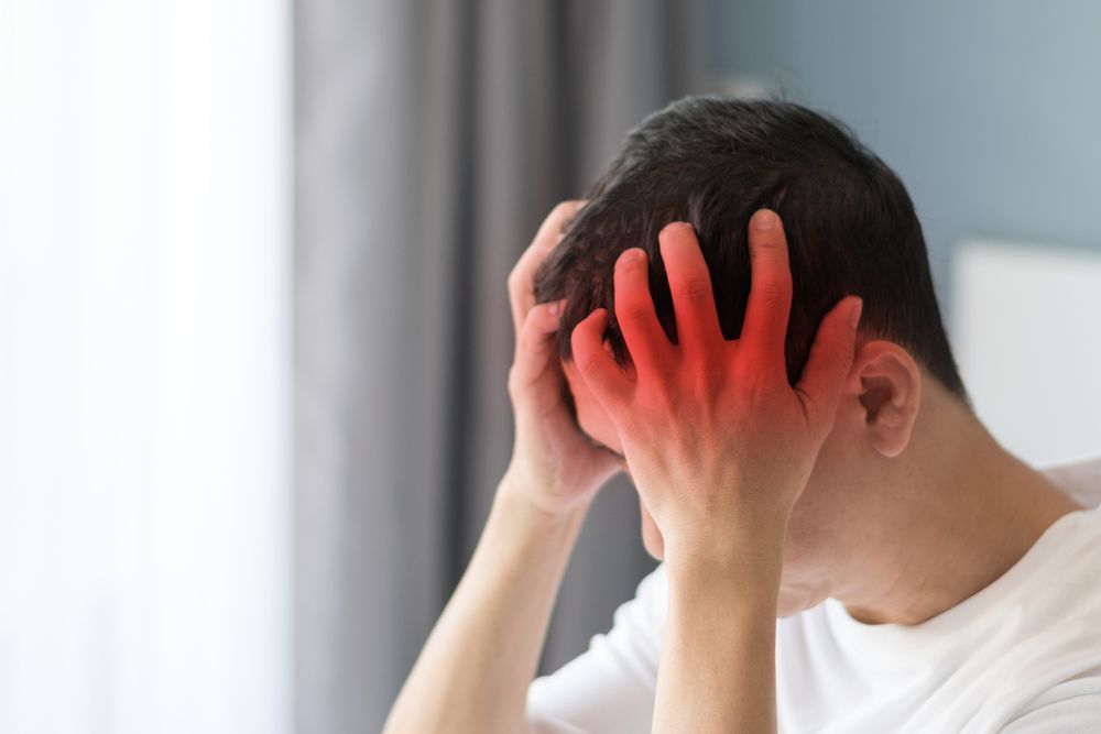 A man is holding his head in pain because of a headache.