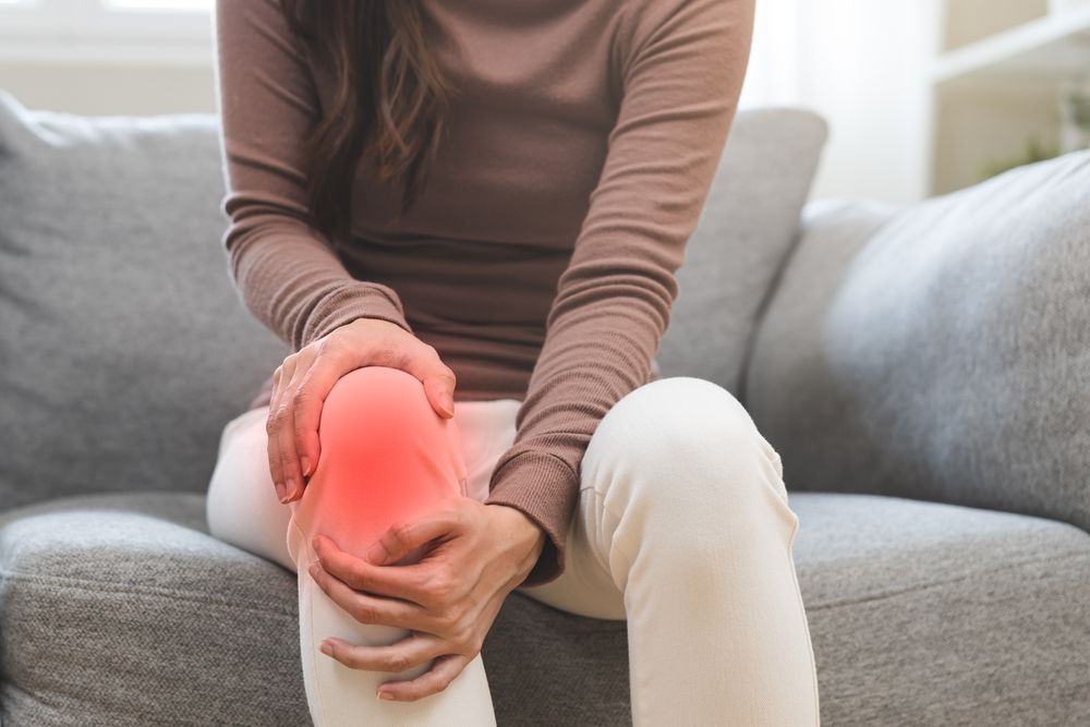 A woman is sitting on a couch holding her knee in pain.