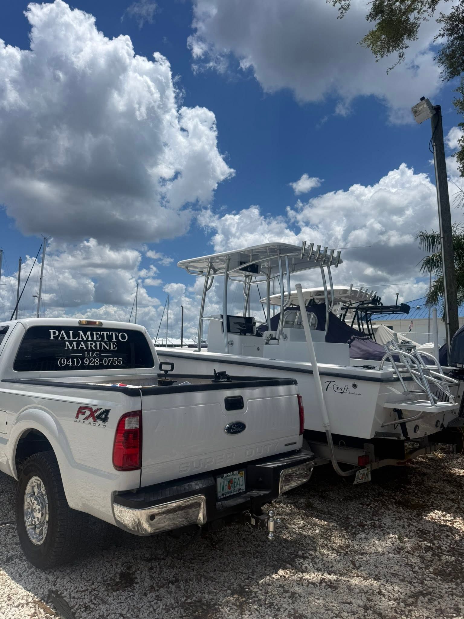 White pickup truck towing a white boat on a trailer under a cloudy blue sky.
