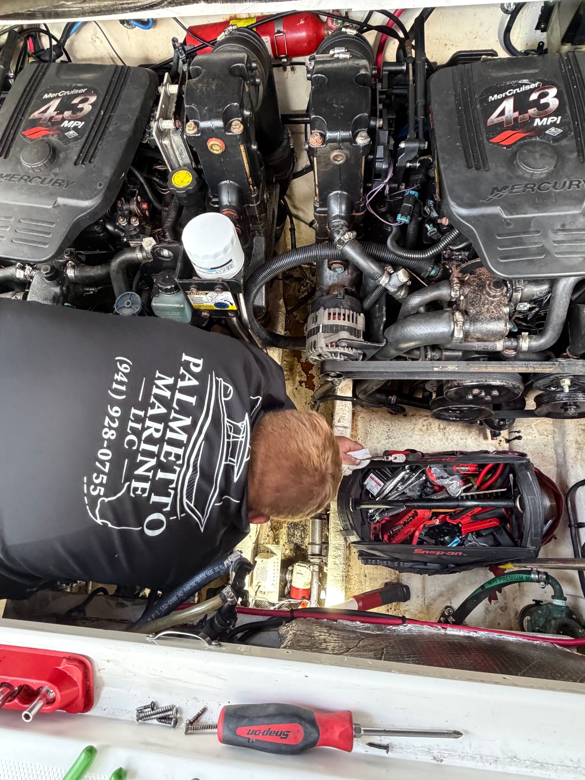 Person working inside a boat engine compartment with twin black engines and red components