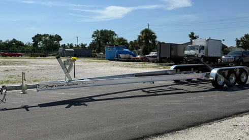 Flatbed semi-trailer parked on an asphalt lot, with trucks and trees in the background.