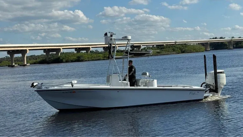 White fishing boat on calm water near a bridge, with one person onboard