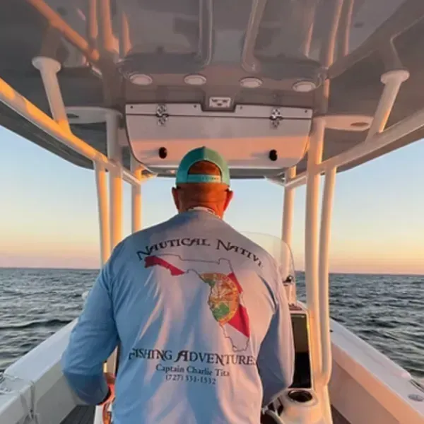 Person steering a boat at sunset on open water, wearing a white shirt and teal cap.